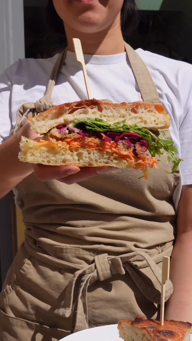 A BRaC. team member holding a colourful focaccia sandwich