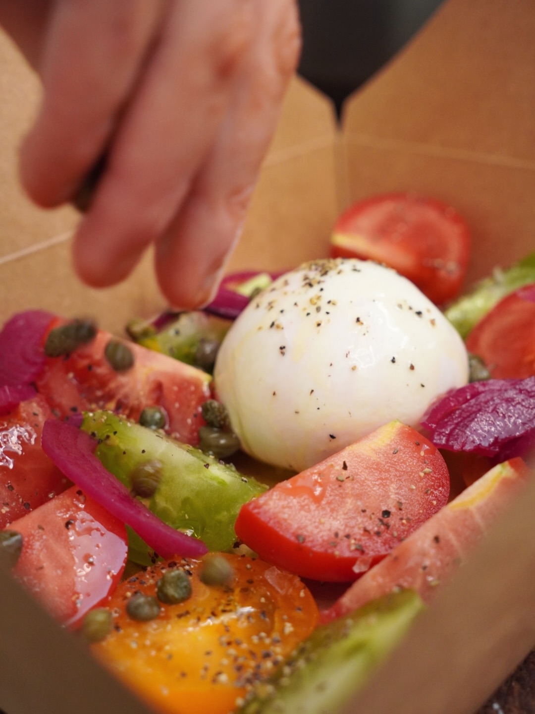 Tomato and burrata salad being seasoned